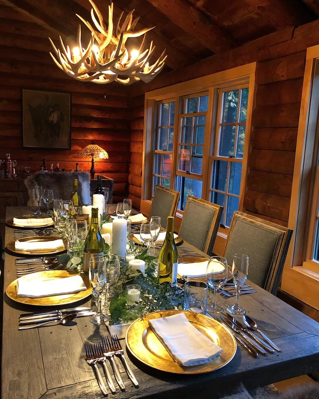 A long dinner table set under an antler chandelier in a log cabin