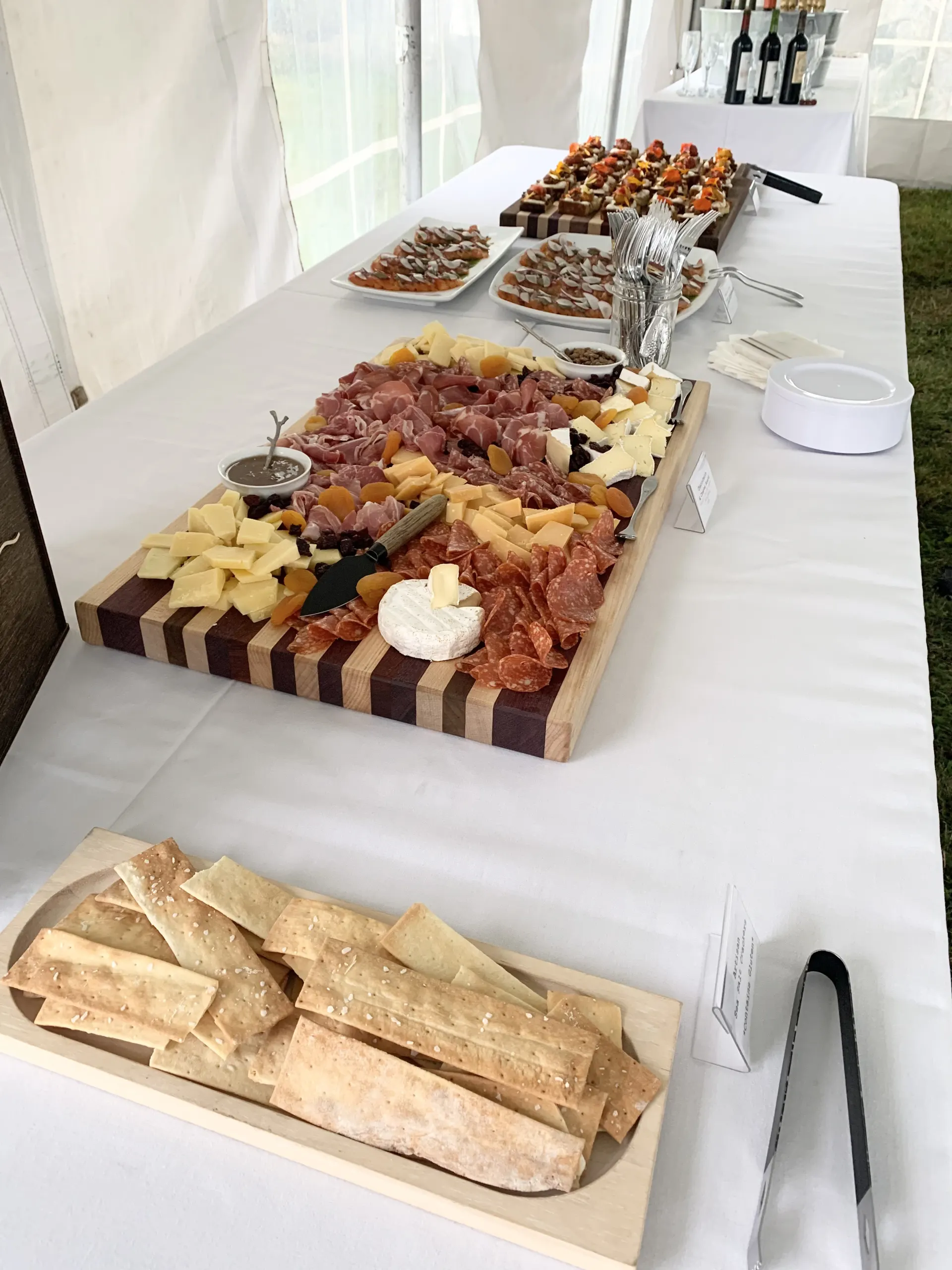 A charcuterie board and canapes on a buffet table under an event tent