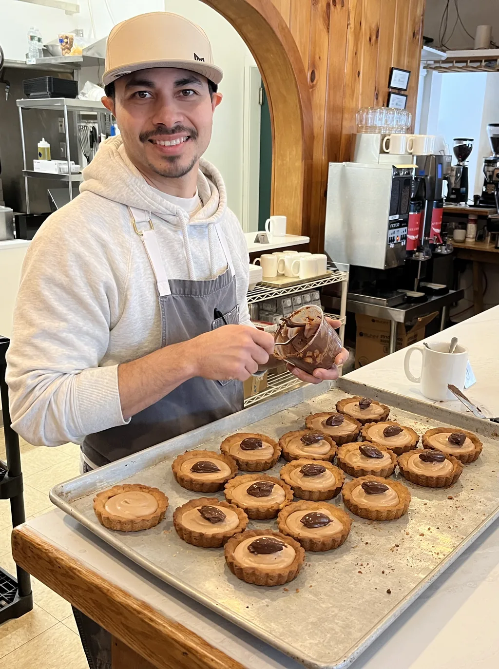 Chef Miguel Calderon smiling behind the counter while finishing a tray of tarts at Alder