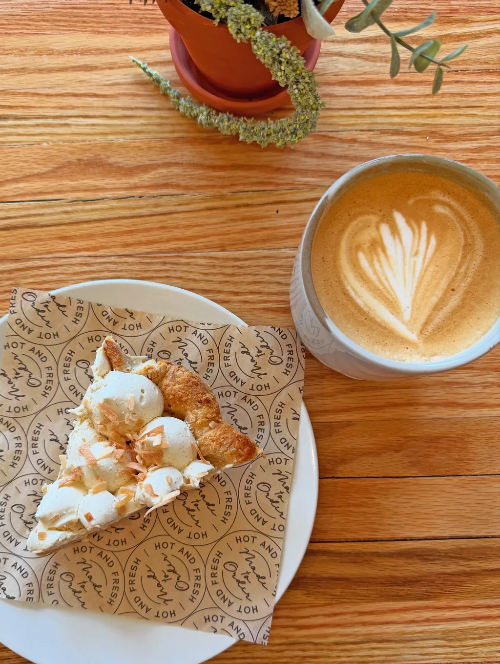 A slice of coconut cream pie beside a latte with heart-shaped latte art