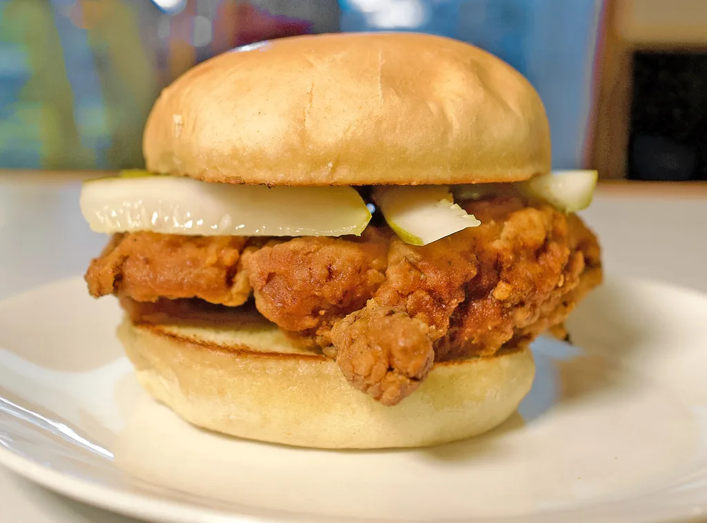 Crispy fried chicken thigh sandwich with sliced pickles on a toasted bun