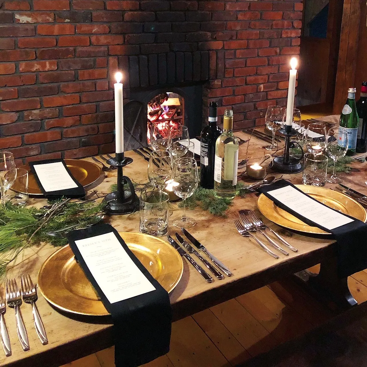 A private dinner table set with candles and printed menus beside a fireplace