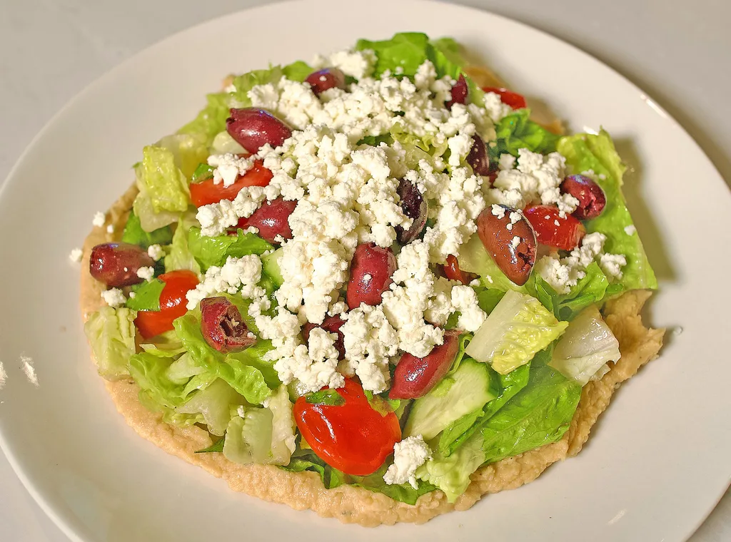 Mediterranean salad with romaine, feta, kalamata olives, tomato and cucumber over chickpea puree